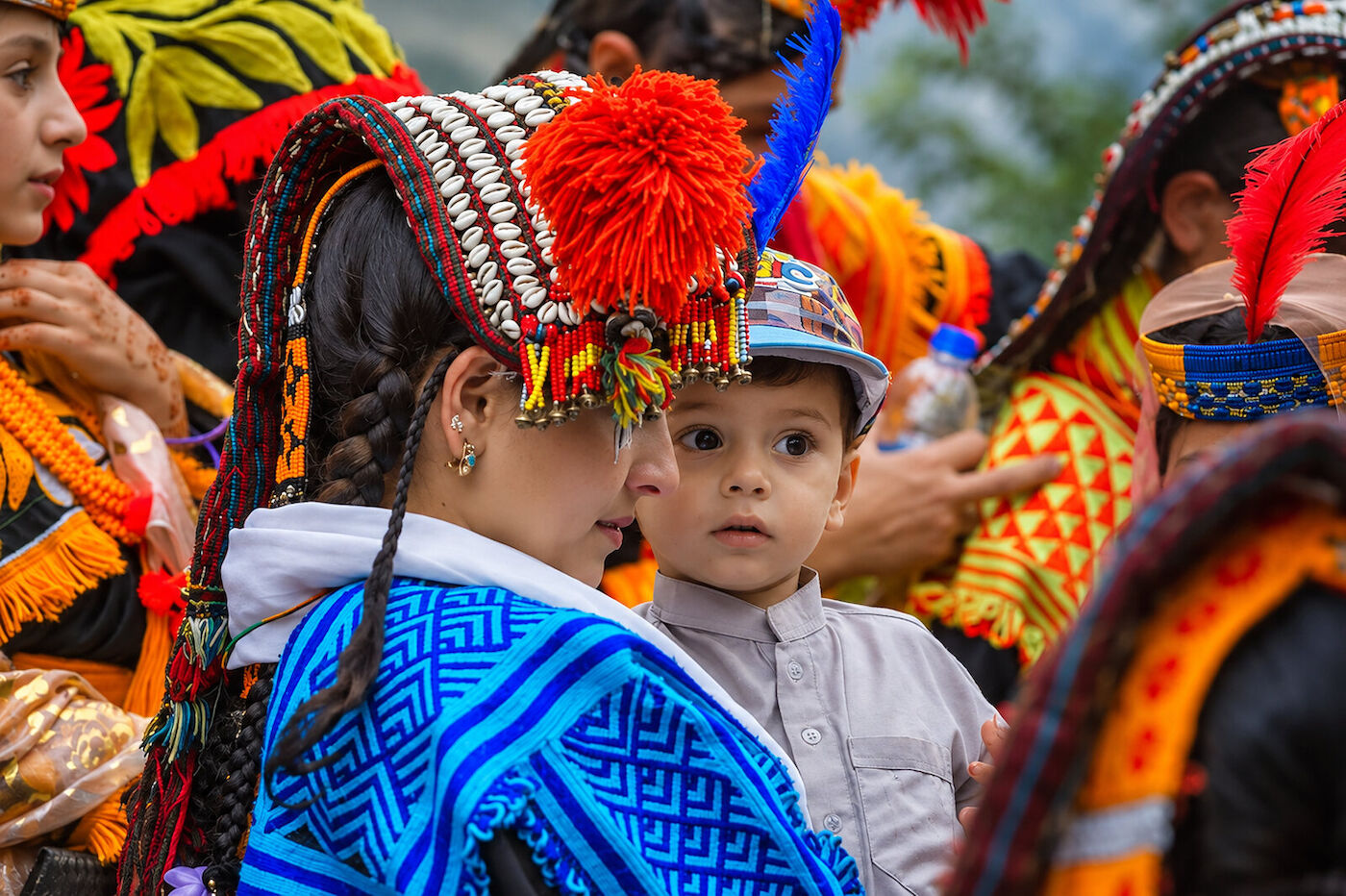 A dense crowd of Kalasha women and children in ceremonial headdresses at a gathering